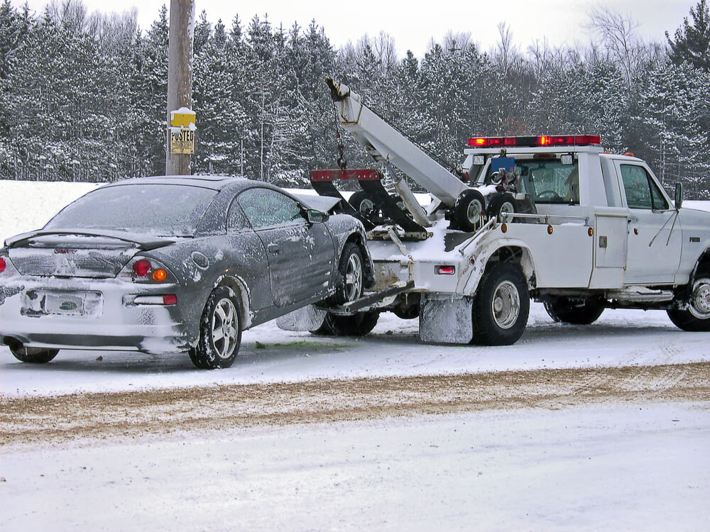 a white pickup truck towing a black car in the snow. - trucks and jeeps