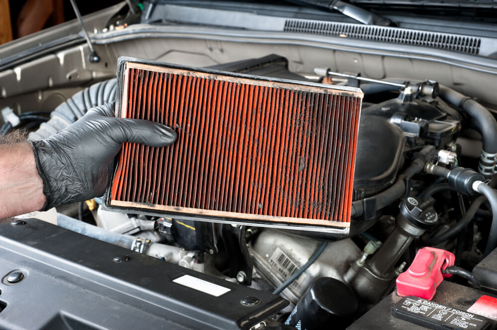 a mechanic holding a dirty air filter - luxury cars bad mileage