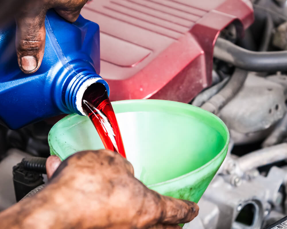 Hand pouring transmission fluid through a funnel as for the good car maintenance - truck leaking red fluid