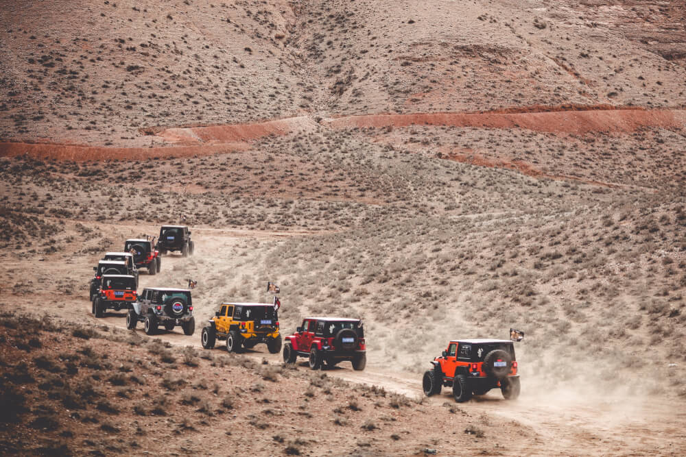 a line of red, orange, and yellow jeeps in a deserted mountainous area. - trucks and jeeps